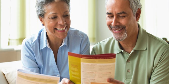 Older couple sits on a couch in a bright room, browsing through estate planning pamphlets together.