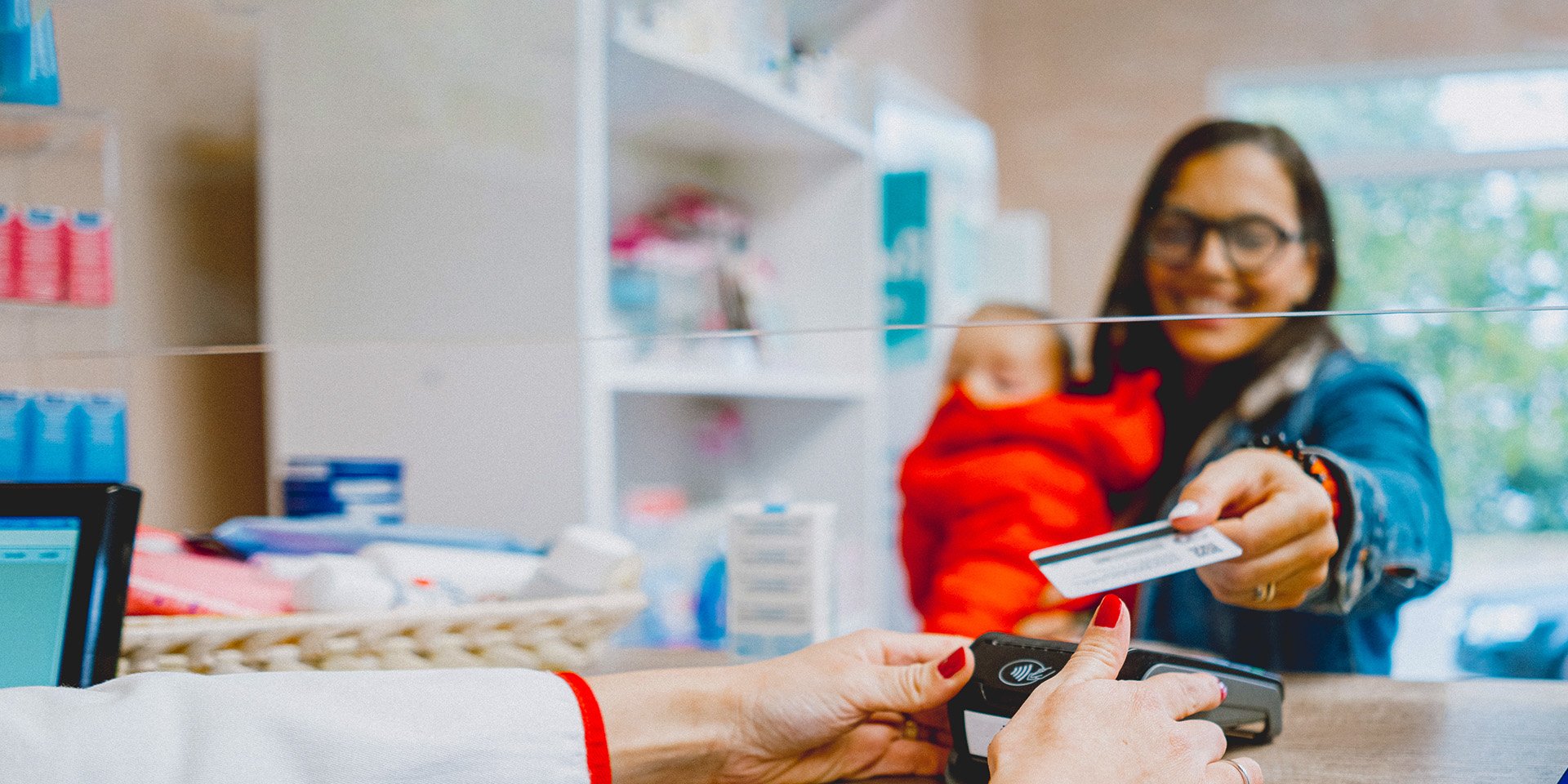 Happy lady holding an infant using her desert financial debit card's tap-to-pay feature at checkout in a store.