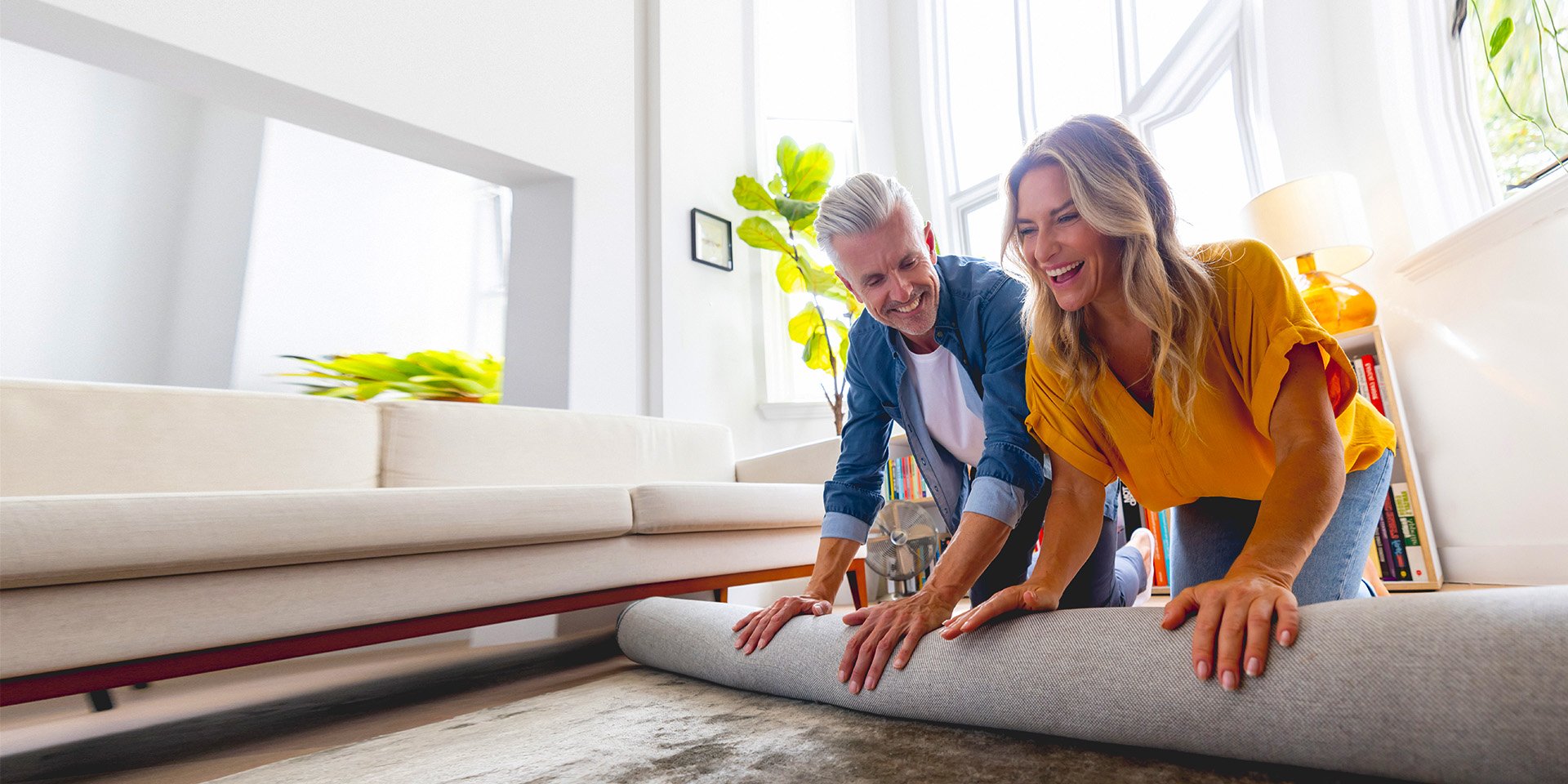 A couple on the floor of their living room excitedly rolling out a new rug on the floor together.