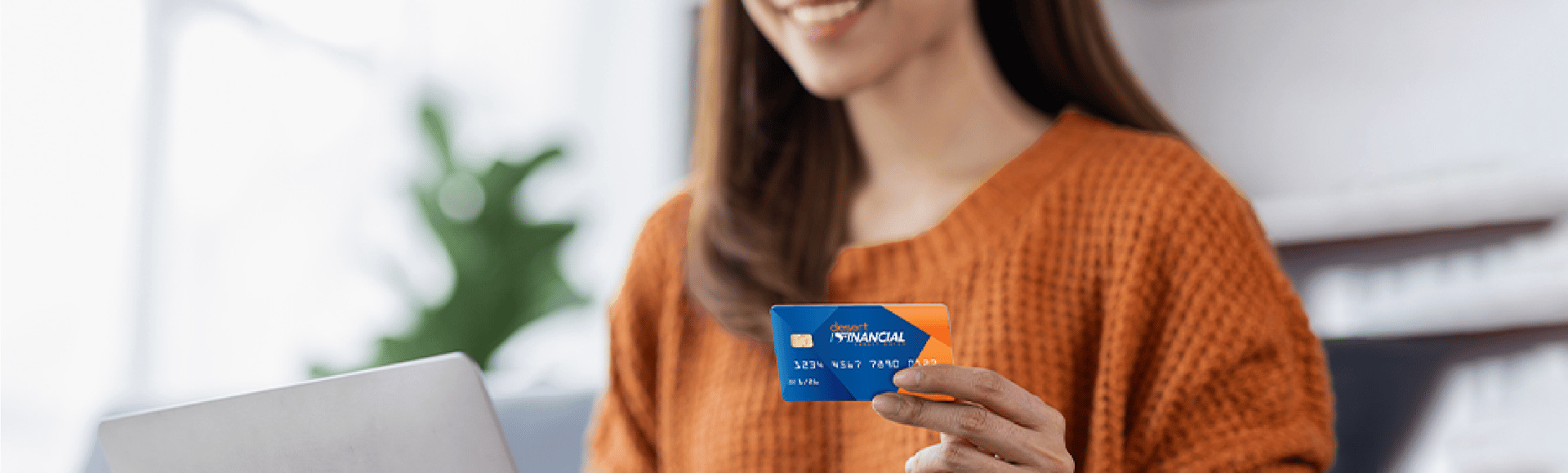 A woman in an orange sweater presents a Desert Financial credit card to the camera.