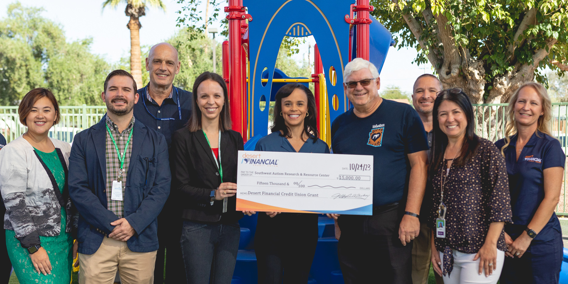 Kevin Haskew, Carlissa Wright, Jeff Meshey, and others joyfully celebrate Desert Financial's generous donation of $15,000 to the Southwest Autism Research & Resource Center. The group proudly displays an enlarged check at an outdoor playground, symbolizing their commitment to community support and philanthropy.