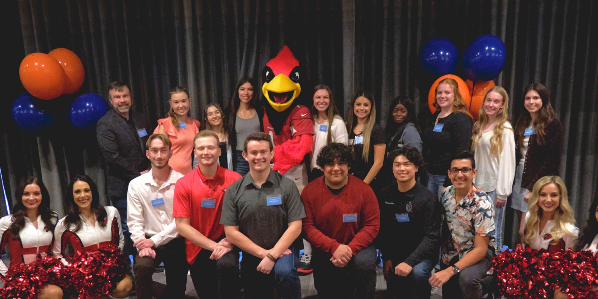 High school student-athletes awarded Desert Financial's scholarship stand with Arizona Cardinals cheerleaders and mascot, Big Red, celebrating their achievements.