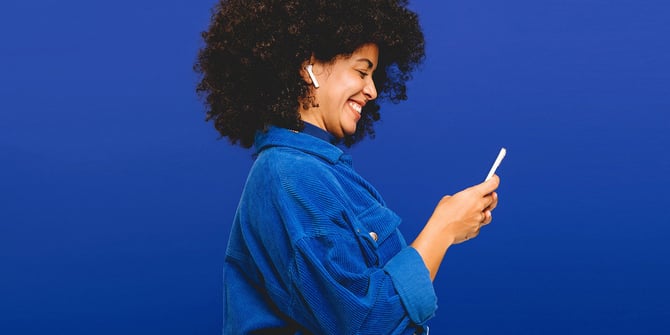 A happy woman in a blue shirt using her smartphone to access the checking features on the Desert Financial mobile banking app.