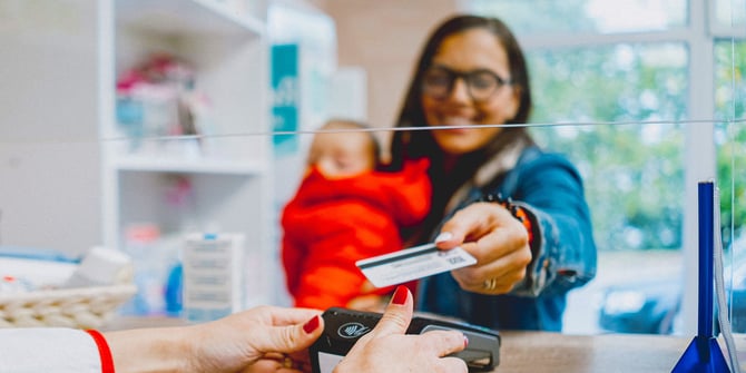 Happy lady holding an infant using her desert financial debit card's tap-to-pay feature at checkout in a store.
