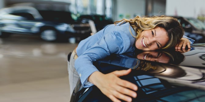 An excited woman hugging the front of her new car inside a car dealership.