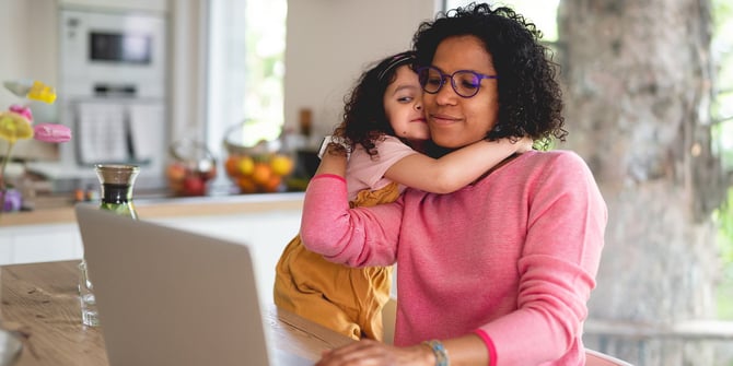 A young daughter embraces her mom warmly at the kitchen table as they find support from Desert Financial, navigating the mortgage assistance process together on their website.