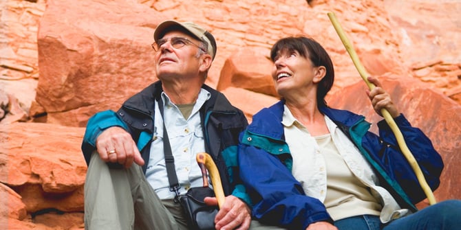 Mature couple rests post-canyon hike, admiring the beauty with walking sticks in hand.