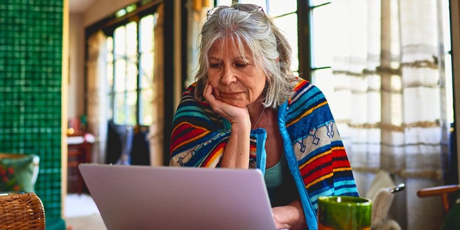 Elderly woman navigates Desert Financial's website, scrolling through the FAQ section on her laptop to find valuable information.