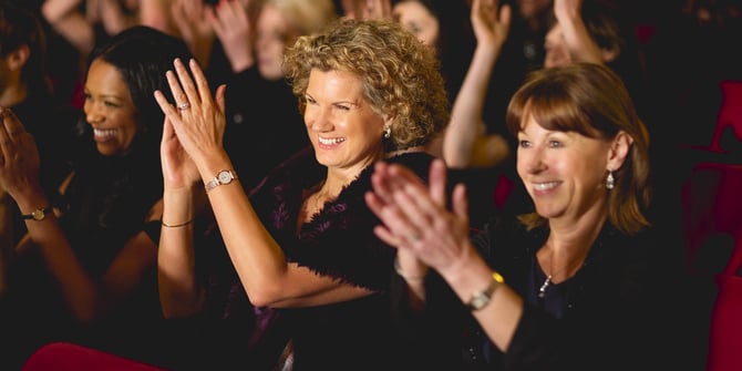 Three enthusiastic ladies join in applause, immersed in a lively crowd at ASU Gammage.