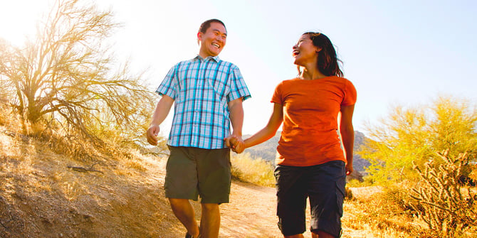Happy couple holding hands while walking down a trail in the desert. 