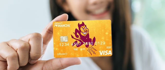 Woman holding up the Desert Financial x Arizona State debit card that is sparkly gold with Sparky the Sun Devil in the center of the card.