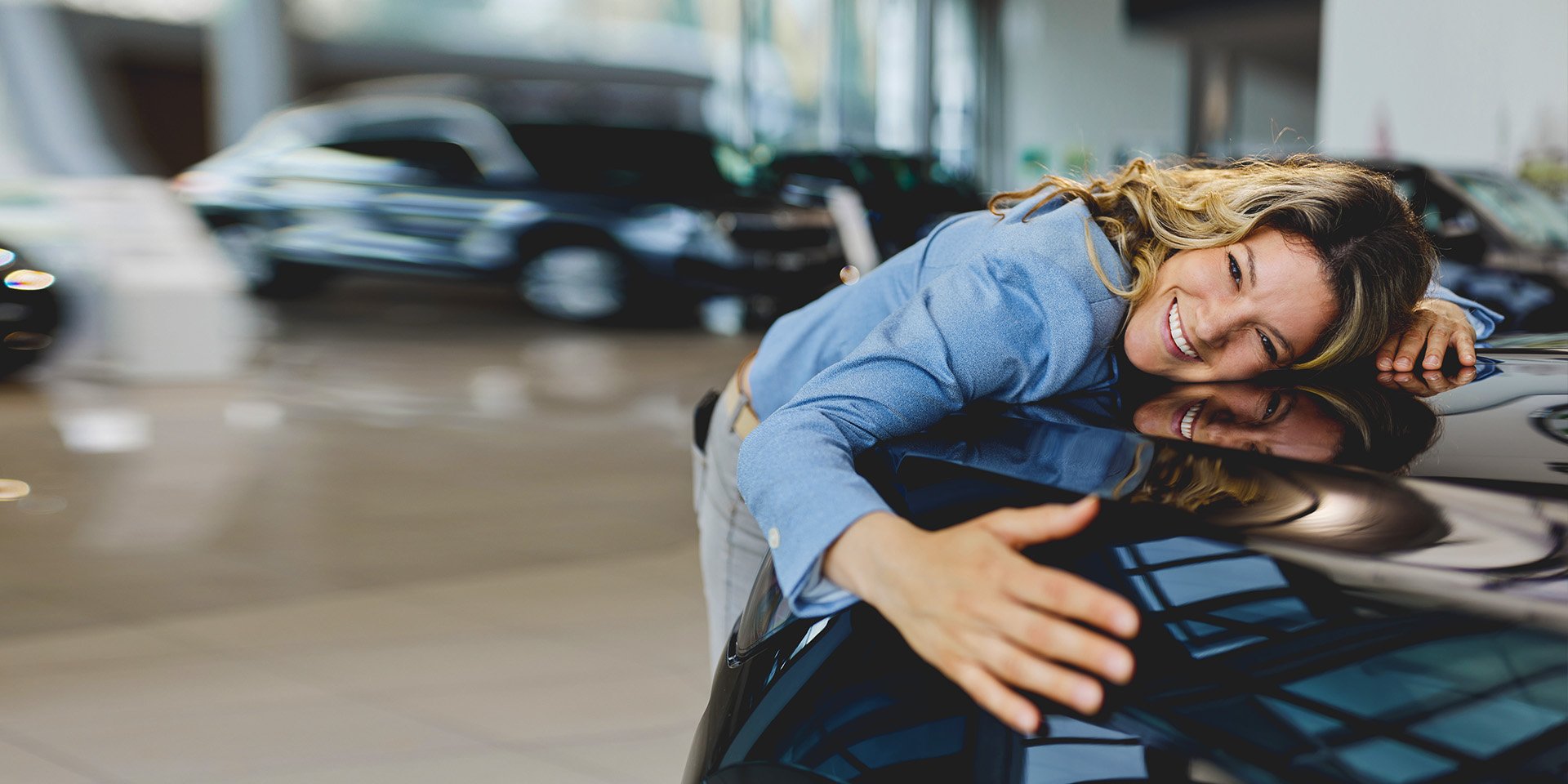 An excited woman hugging the front of her new car inside a car dealership. An excited woman hugging the front of her new car inside a car dealership.