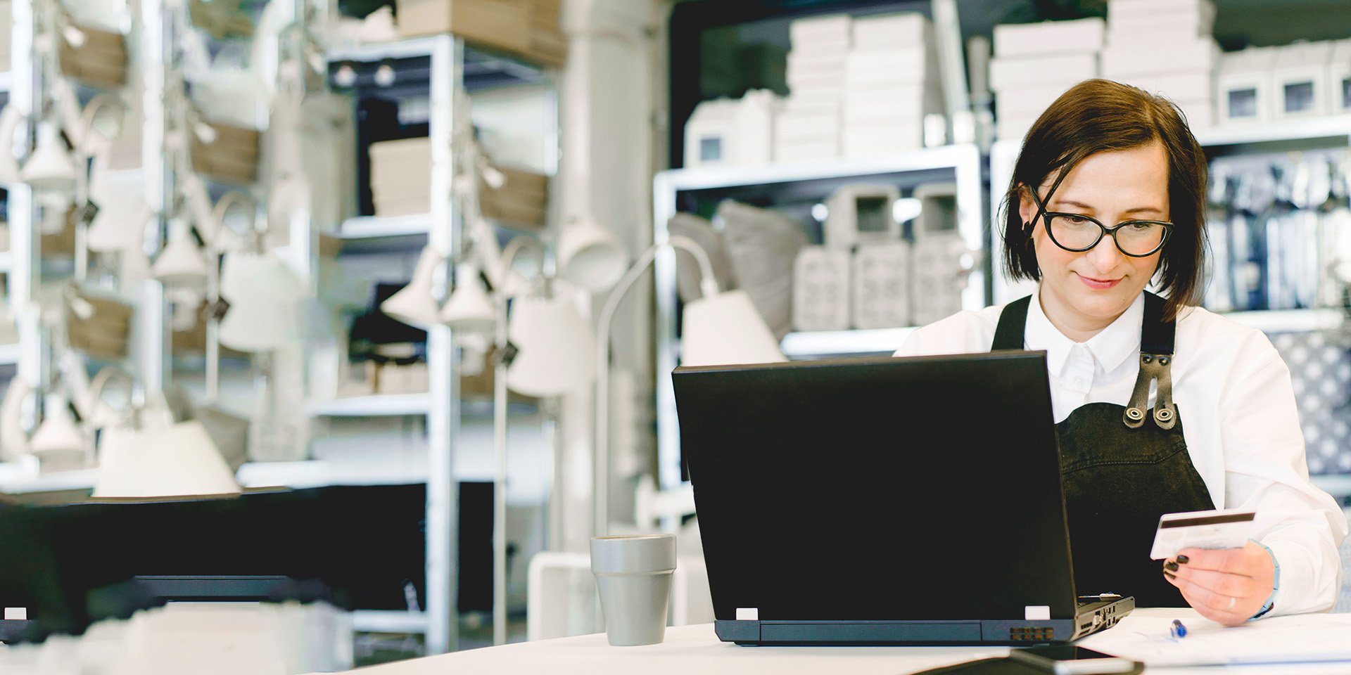 A store owner in an apron securely enters her business' Desert Financial credit card information into a laptop behind the counter. A store owner in an apron securely enters her business' Desert Financial credit card information into a laptop behind the counter.