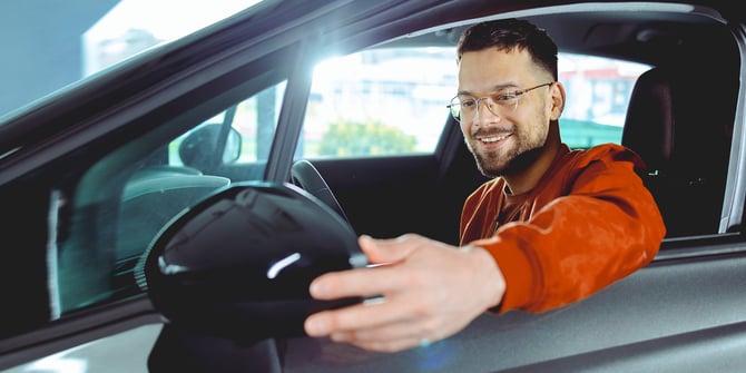 A new graduate sitting in the driver's seat of his car and fixing the side mirror through the window. A new graduate sitting in the driver's seat of his car and fixing the side mirror through the window.