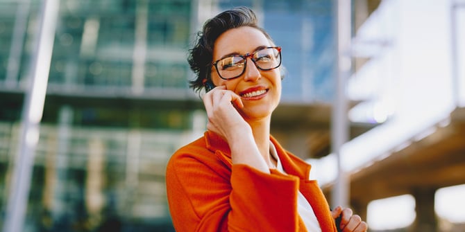 A happy businesswoman with glasses who is on the phone outside.