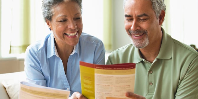 Older couple sits on a couch in a bright room, browsing through estate planning pamphlets together. Older couple sits on a couch in a bright room, browsing through estate planning pamphlets together.
