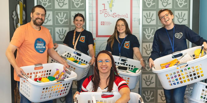 Five Desert Financial employees, each holding laundry baskets filled with cleaning supplies, contribute to the support of Phoenix Children's Hospital's 1 Darn Cool School.