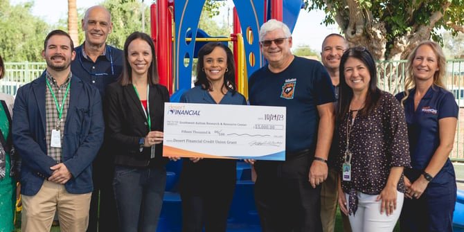 Kevin Haskew, Carlissa Wright, Jeff Meshey, and others joyfully celebrate Desert Financial's generous donation of $15,000 to the Southwest Autism Research & Resource Center. The group proudly displays an enlarged check at an outdoor playground, symbolizing their commitment to community support and philanthropy.